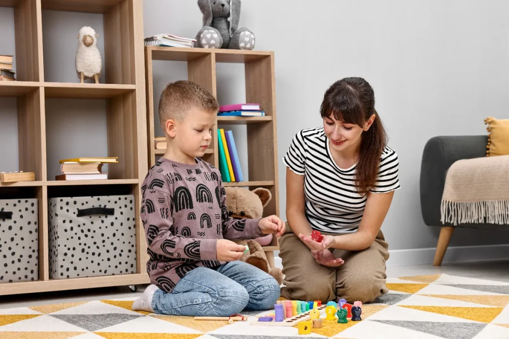 Educadora e aluno sentados no chão interagindo com blocos de montar coloridos, ilustrando a aplicação de práticas pedagógicas lúdicas na educação inclusiva.